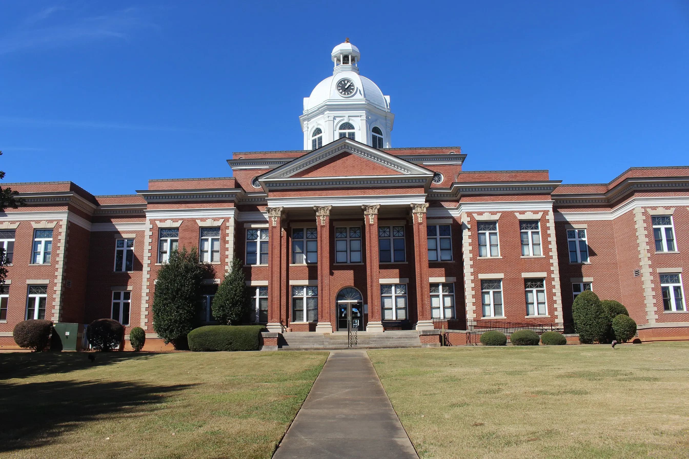 The Putnam County Courthouse in Eatonton, Georgia: a red-brick building with a white columned portico and cupola under a clear blue sky.