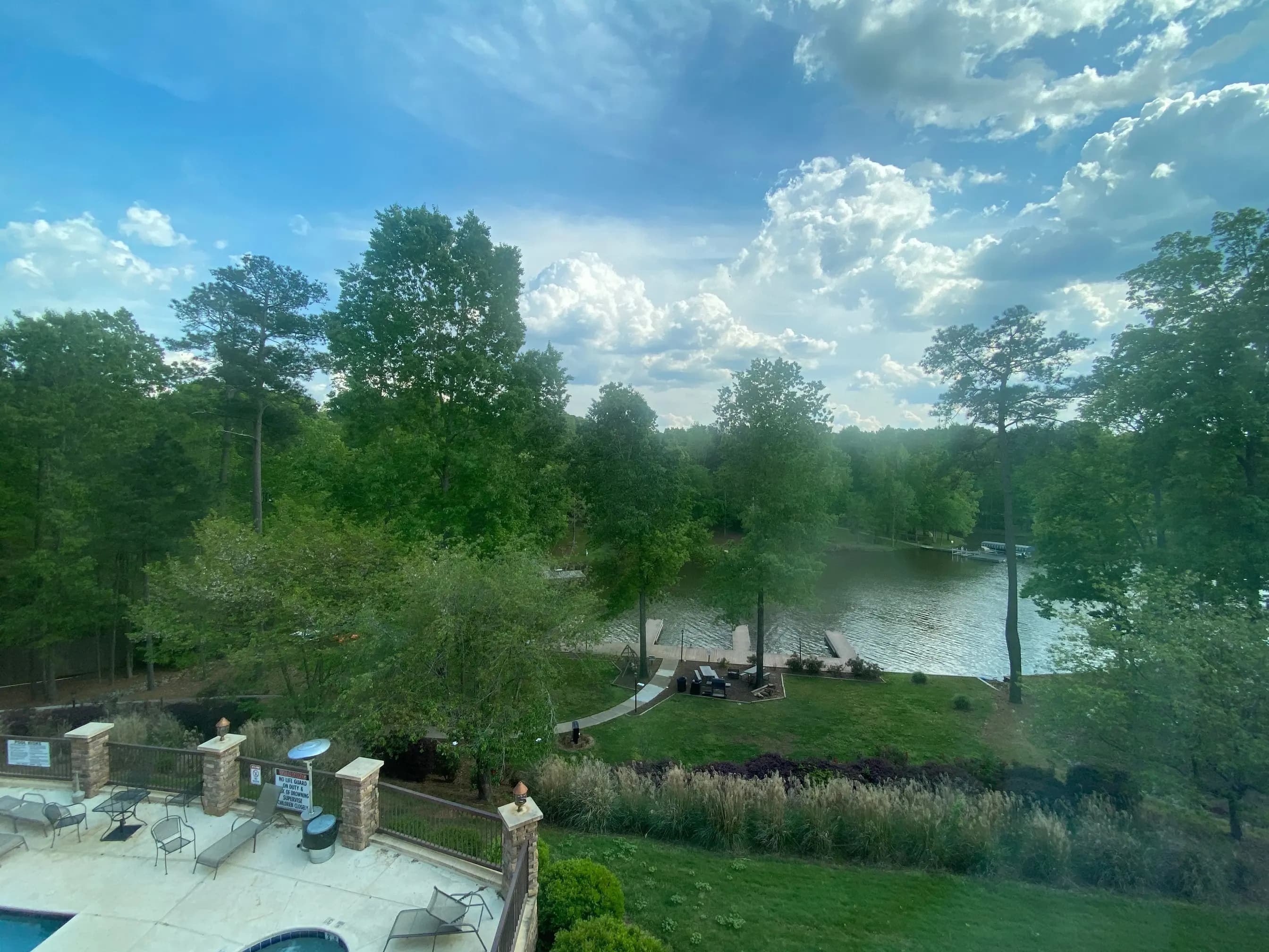 A wooded Lake Oconee cove with a dock and lawn, seen over a stone terrace under a big summer sky.