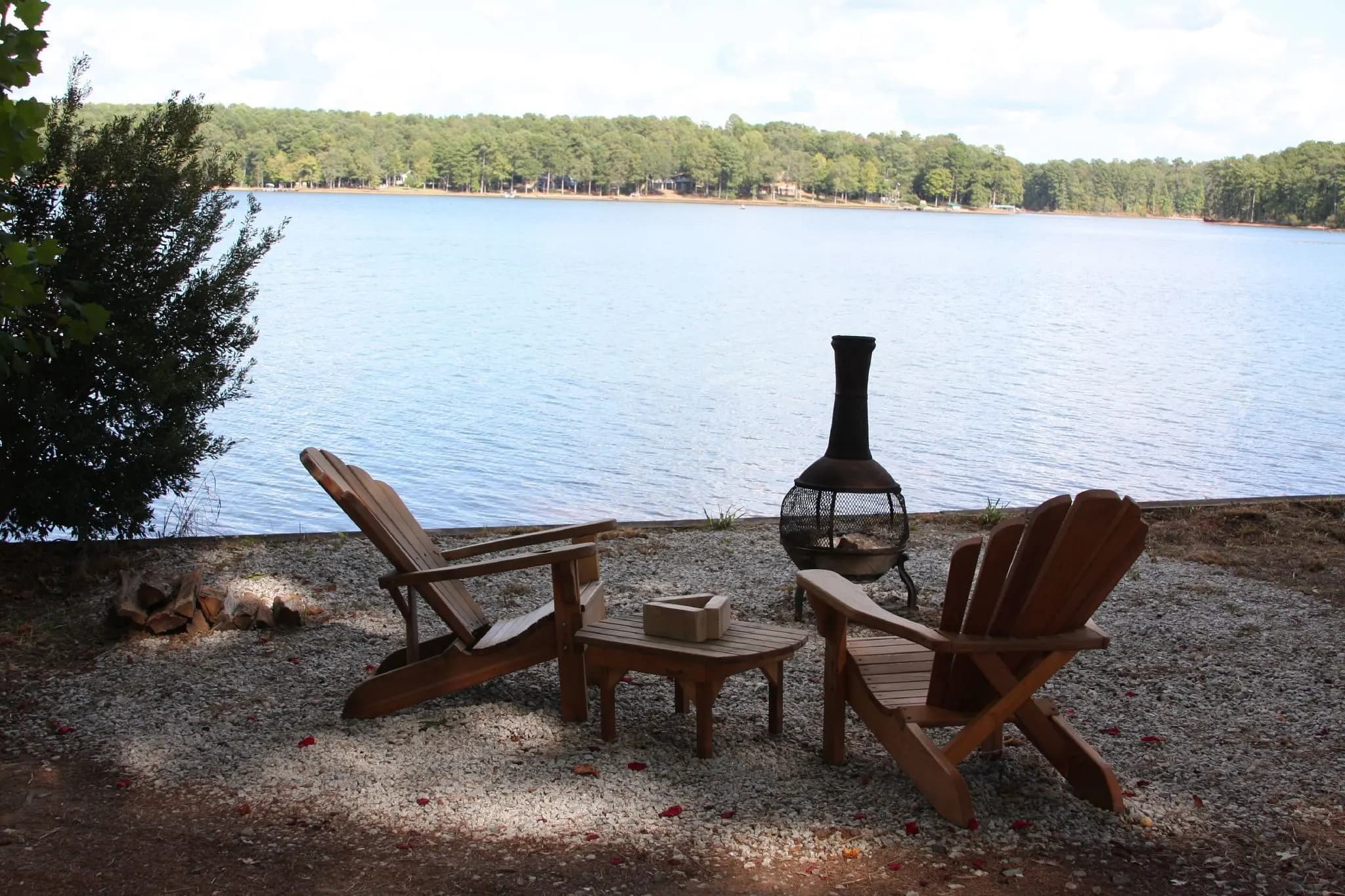 Adirondack chairs and a chiminea on a gravel pad above the open water of Lake Oconee, a wooded shoreline across the lake.