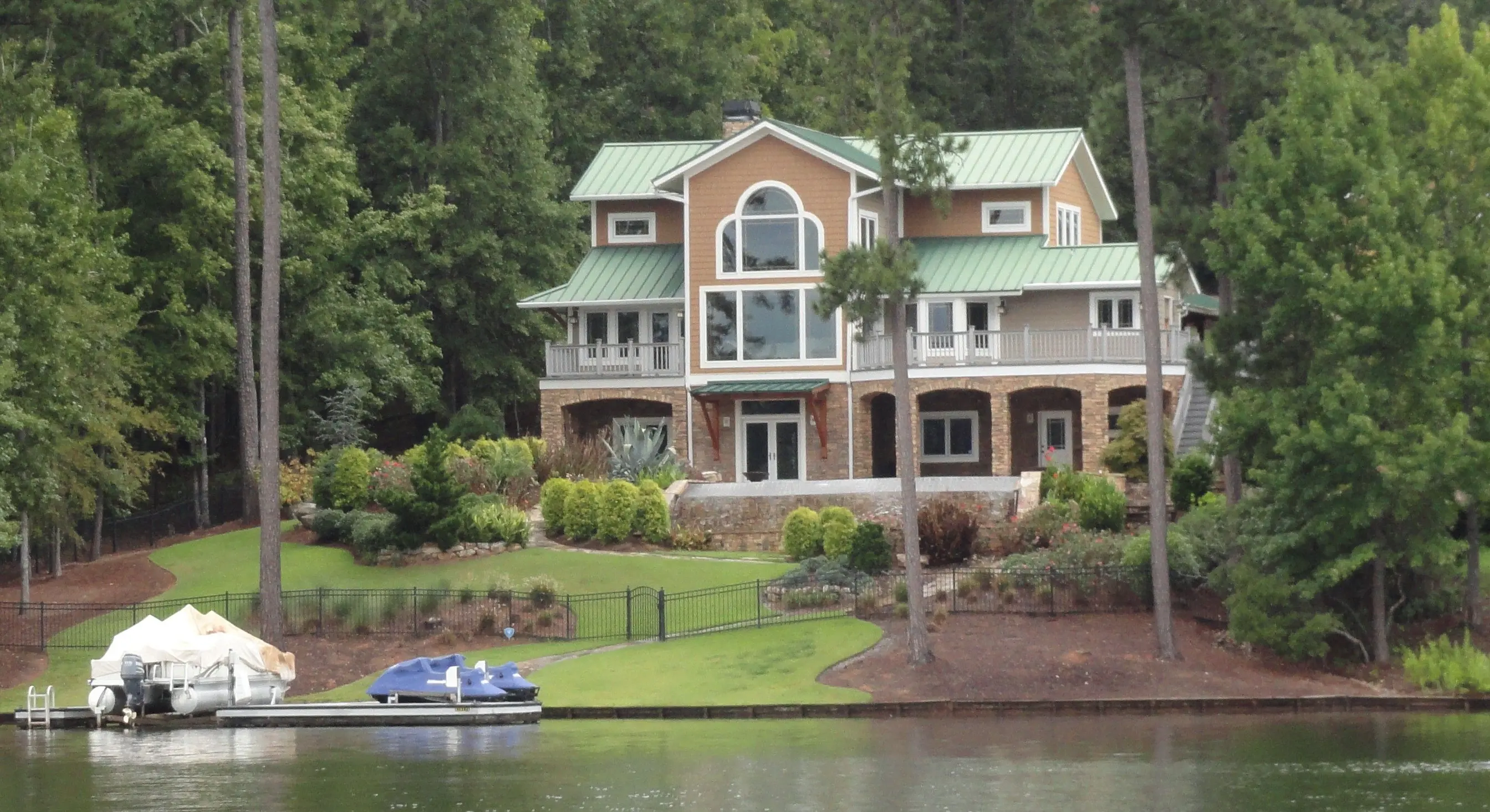 A lake house with a green metal roof on a pine-wooded slope above a boat dock on Lake Oconee.
