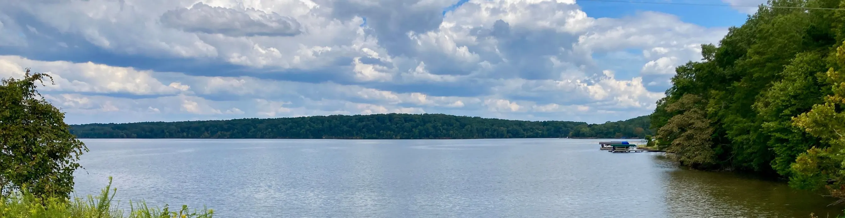 Open water on Lake Oconee under puffy summer clouds, a low wooded ridge and a dock on the far shore.