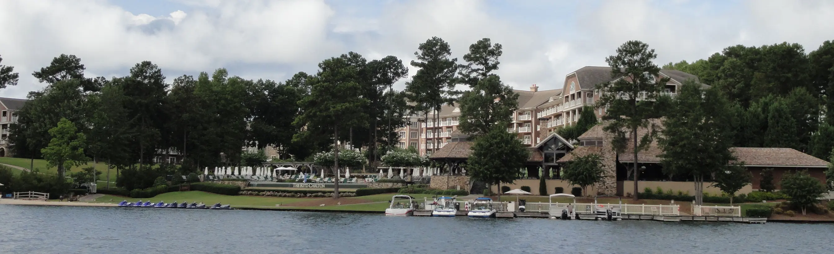 A wide panorama of the wooded Lake Oconee shoreline with a lodge, docks and boats along the water.