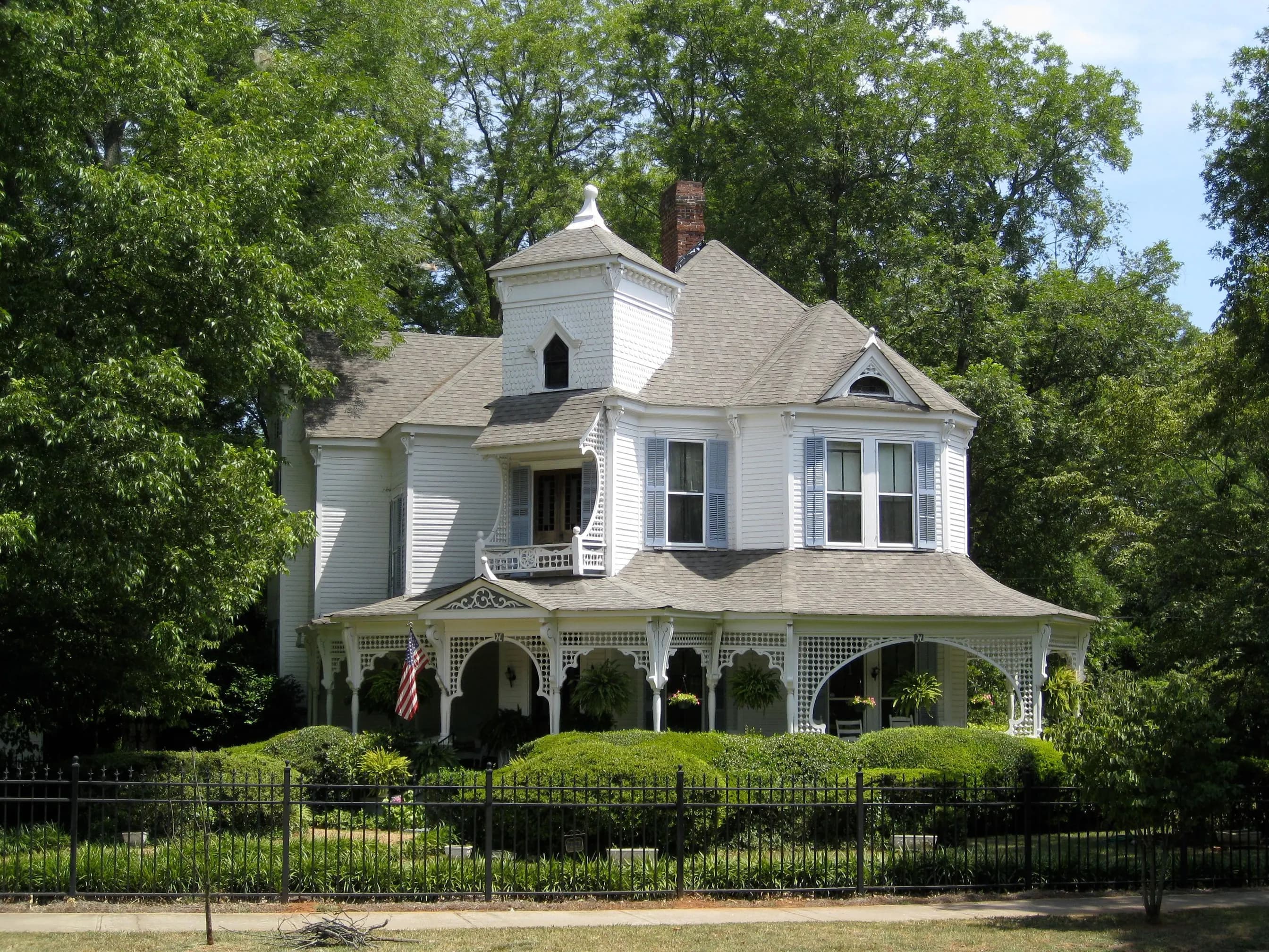 A white Victorian house with a wraparound porch behind an iron fence in historic Madison, Georgia.
