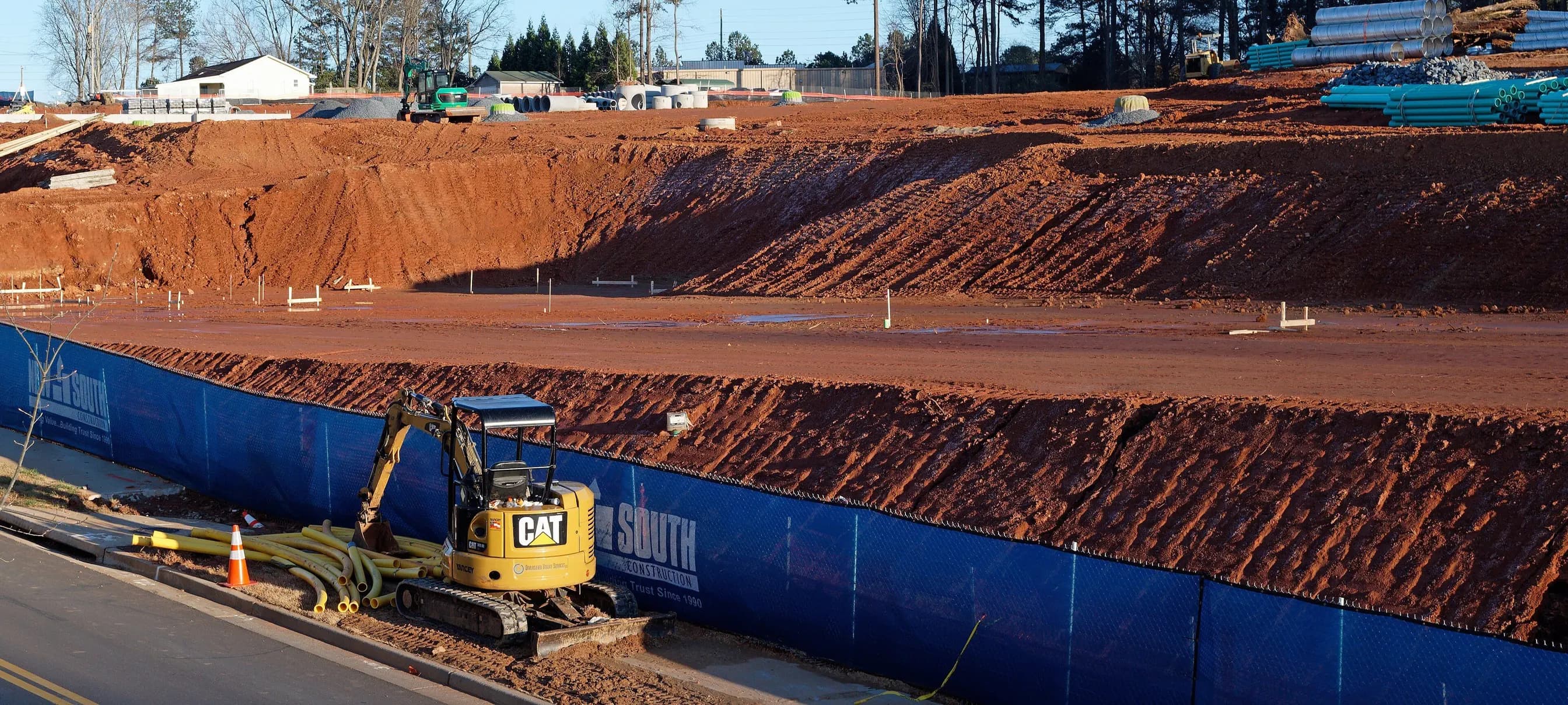 A deep cut of Georgia red clay at a graded construction site, a compact excavator parked at its foot.