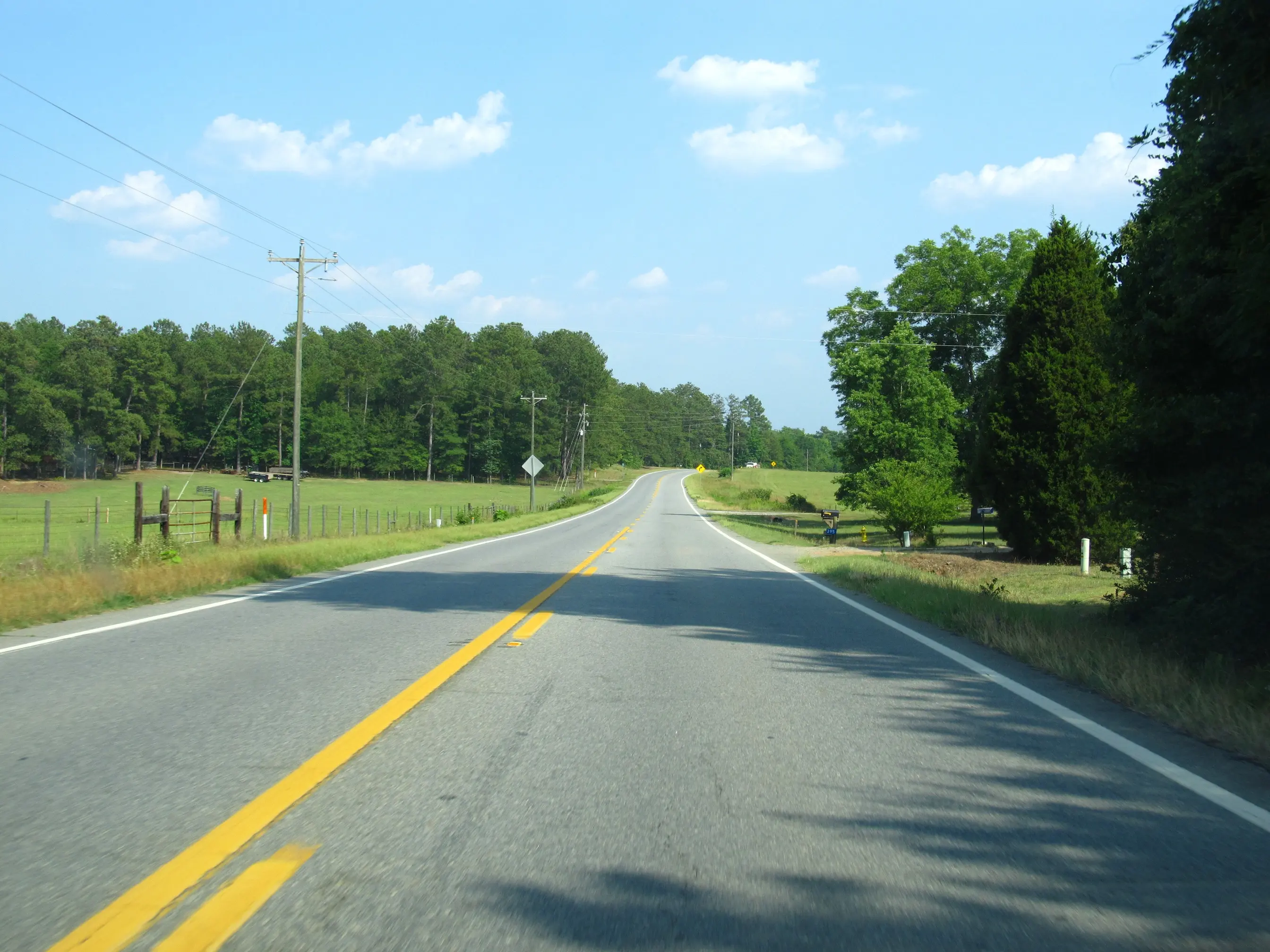 A two-lane highway curving past fenced pasture and pine woods in rural Middle Georgia between Milledgeville and Sandersville.