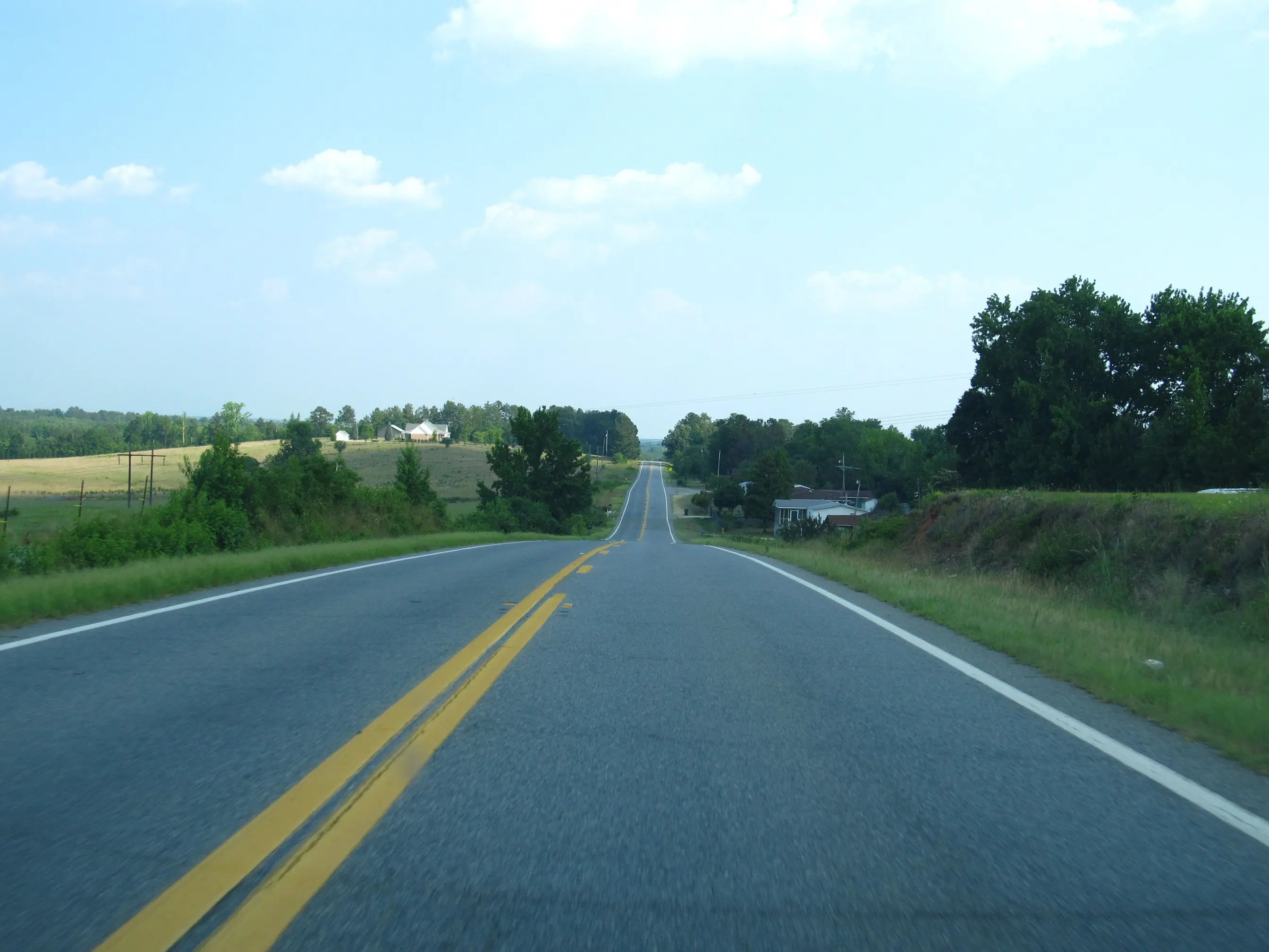 A two-lane highway running over rolling Piedmont farmland with hayfields and tree lines in rural Middle Georgia.